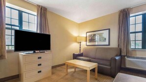 A hotel room with a flat-screen TV, a sofa, a table, a lamp, and a framed picture on the wall.
