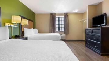 A hotel room with two beds, a television, a dresser, a window with curtains, and a lamp.