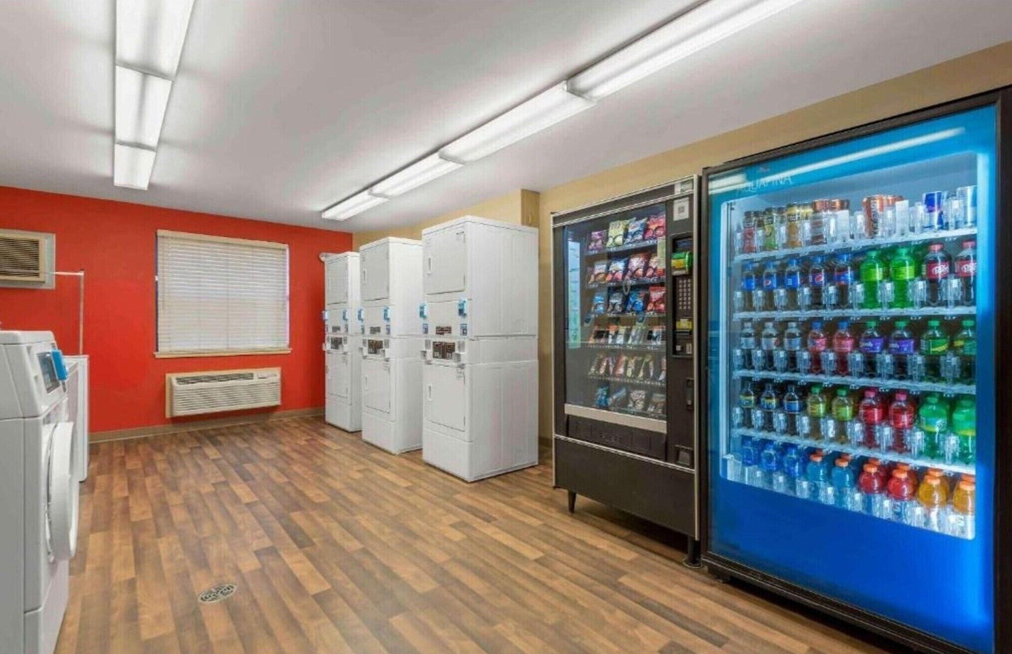 Une pièce dotée d’un plancher en bois, d’un distributeur automatique proposant diverses boissons et d’appareils électroménagers blancs empilés.