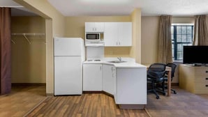 Eine kompakte Küche mit Kühlschrank, Mikrowelle und Spüle, ein kleiner Arbeitsbereich mit Schreibtisch und Stuhl sowie ein Fernseher.