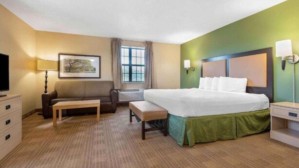 Ein Hotelzimmer mit Bett, Schreibtisch, Stuhl, Fernseher, Fenster und einem Bild an der Wand.