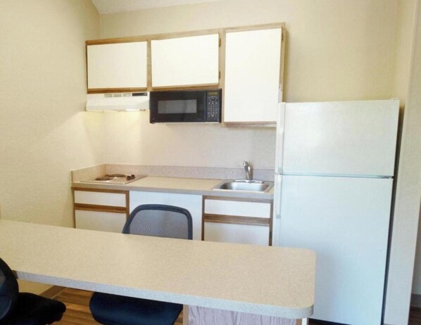 Una cocina compacta con microondas, refrigerador, lavabo y un pequeño comedor con una silla.