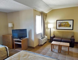 Ein Hotelzimmer mit Bett, Fernseher, Sofa, kleinem Tisch, Lampe und einem gerahmten Bild an der Wand.