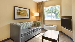 Habitación de hotel con sofá, televisión de pantalla plana, lámpara y ventana con vistas a árboles y un vehículo afuera.