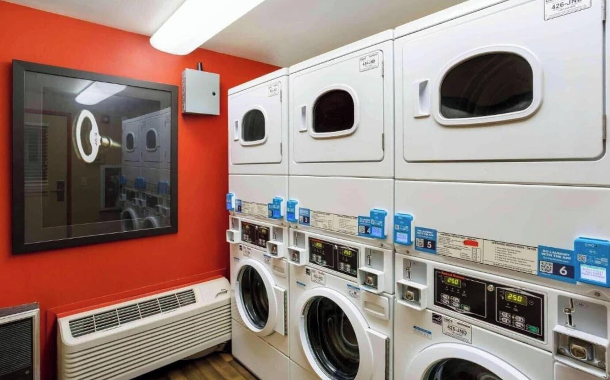 A laundry facility with multiple washing machines, a ventilation system, and a large mirror.