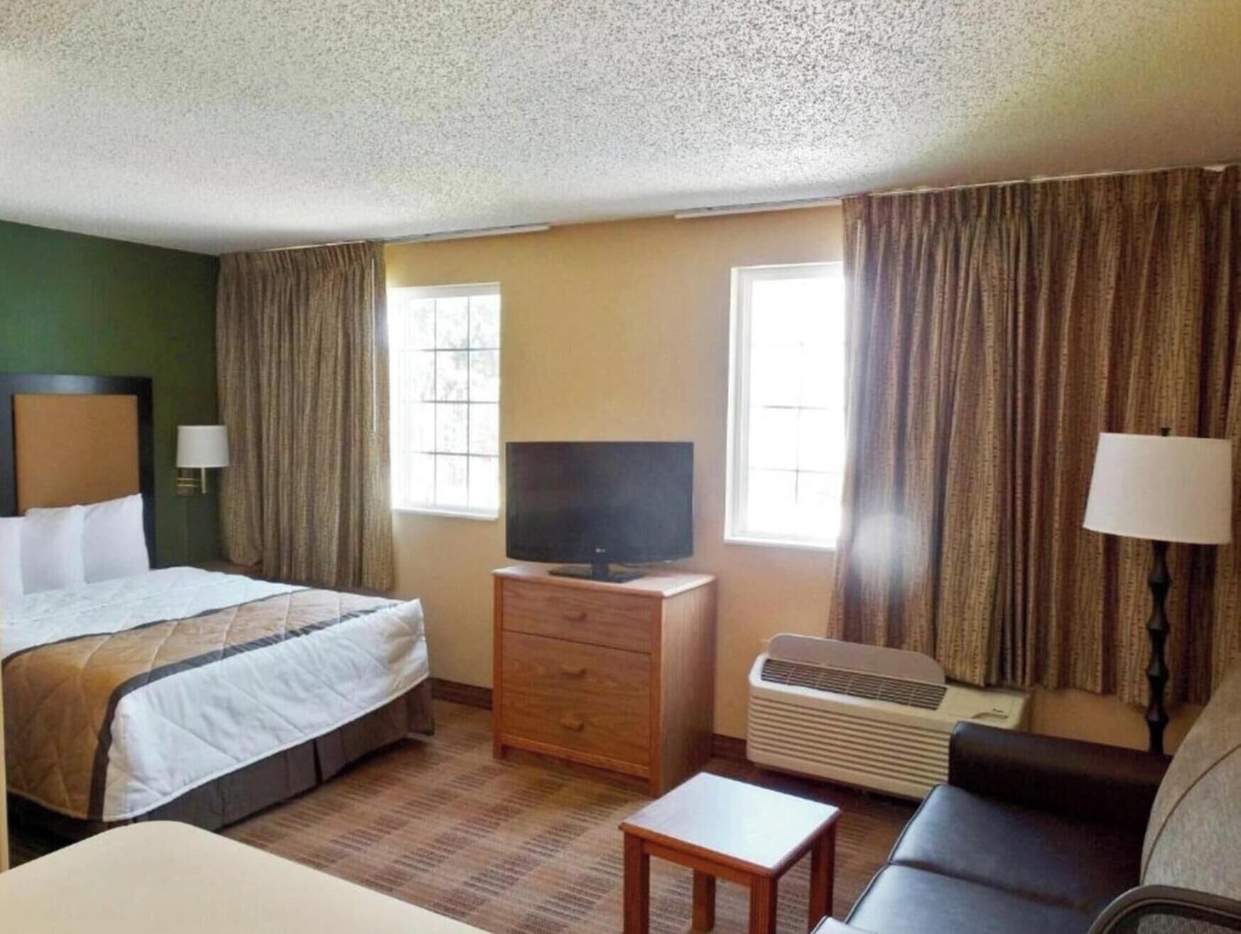 Ein Hotelzimmer mit einem Bett, einem Fernseher, einem Schminktisch, einer Couch und einer Klimaanlage.