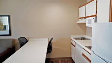 A compact kitchen with a white countertop, a microwave, a stove, and a refrigerator.