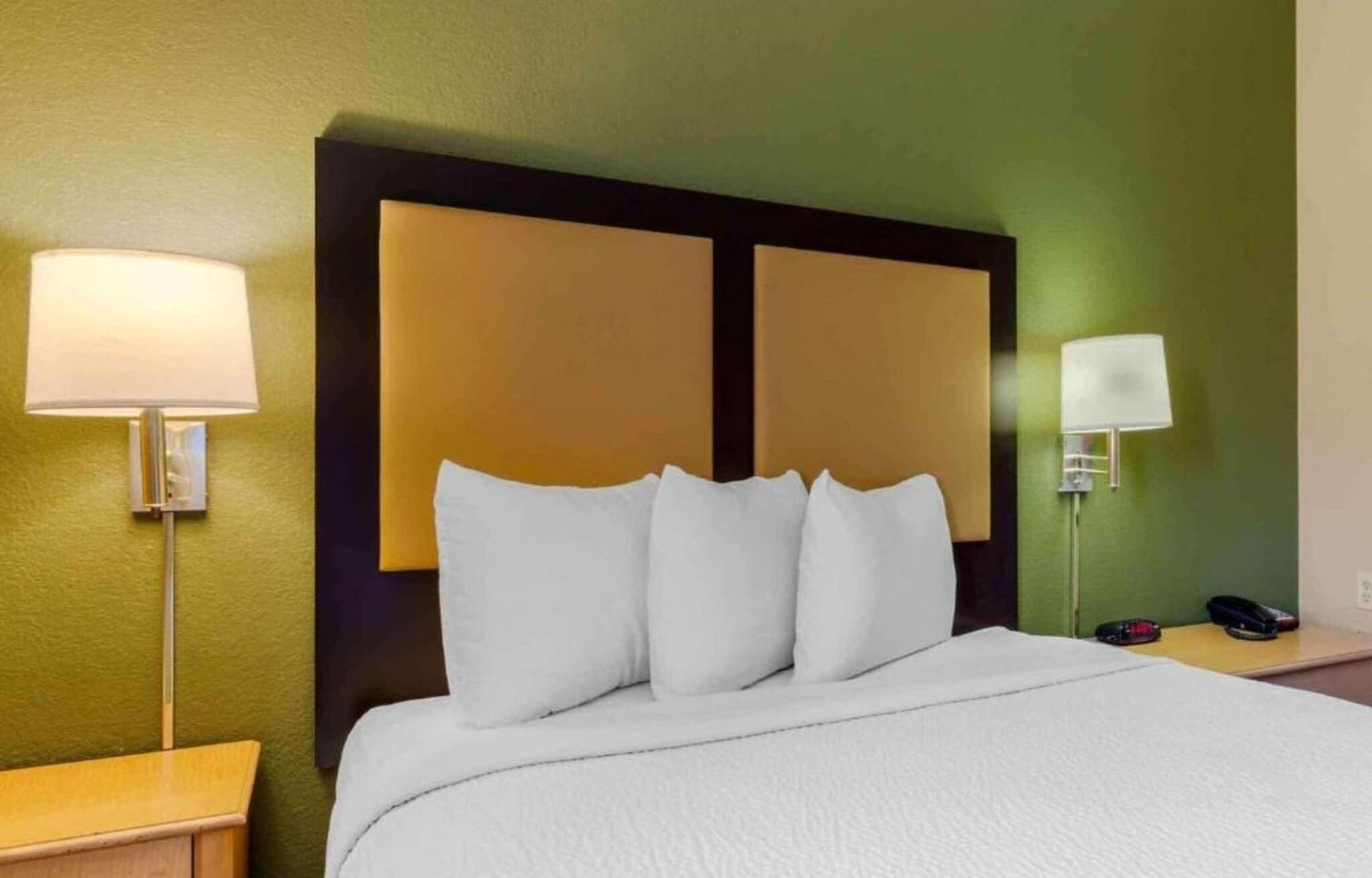 Habitación de hotel con cama, dos lámparas de noche, una mesita de noche y teléfono instalado en la pared.