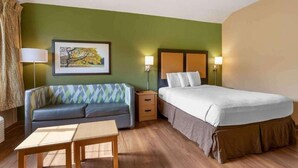 A hotel room with a bed, a sofa, a table, and a painting on the wall.