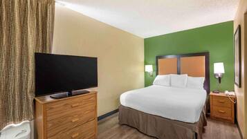 A hotel room with a bed, a TV on a wooden dresser, a nightstand with a lamp, and a green accent wall.