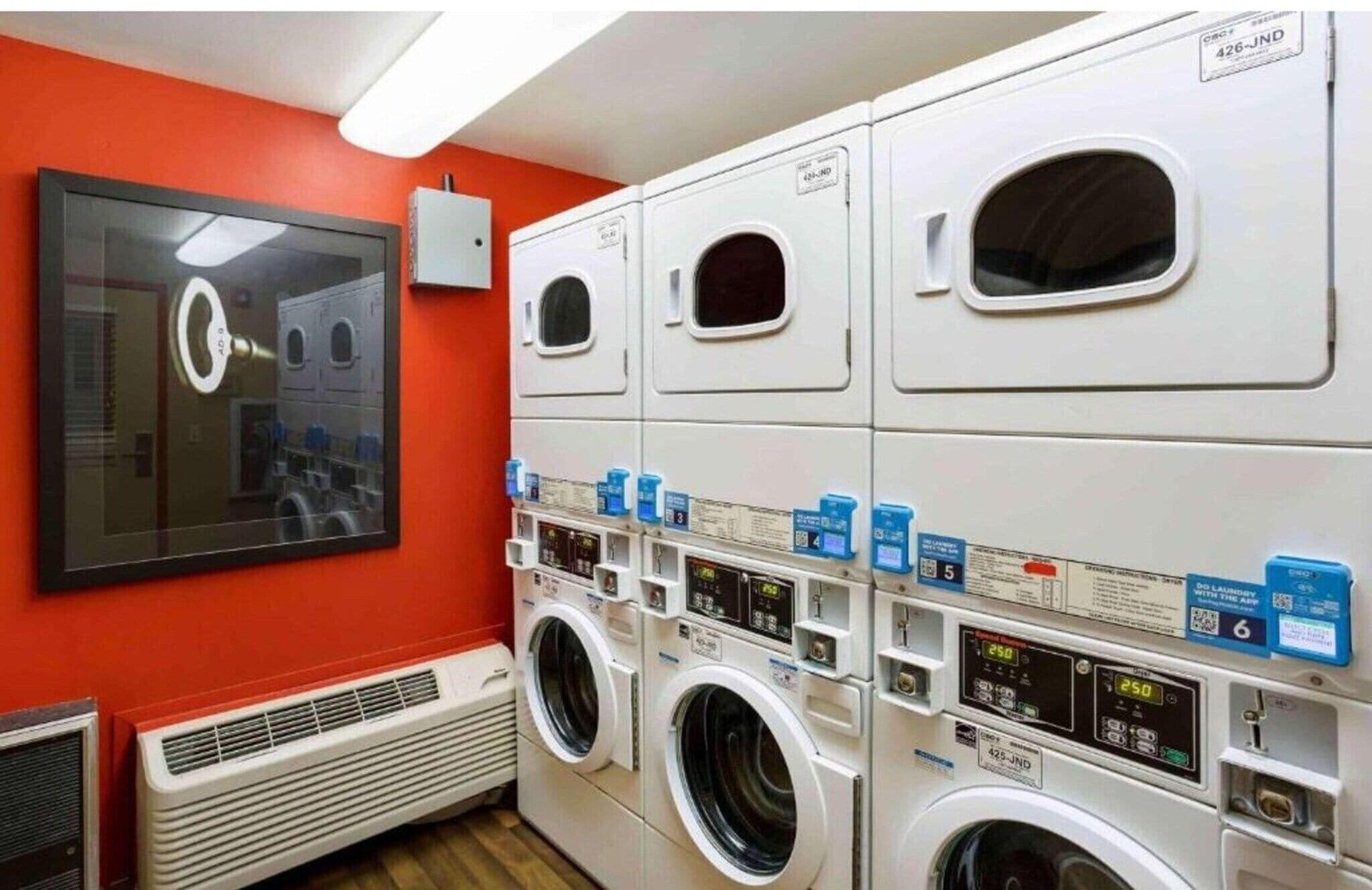 Een wasserette met meerdere wasmachines, een ventilatiesysteem en een grote spiegel.