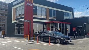 Ein McDonald's Restaurant mit Drive-In, davor ein schwarzes Auto und eine Person in der Nähe des Eingangs.