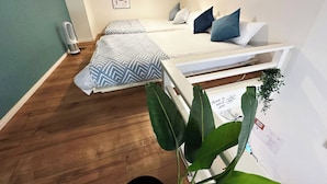 Ein Schlafzimmer mit zwei Betten, einem Nachttisch, einem Wandbild und einer Pflanze.