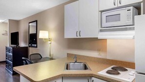 A compact kitchenette with a microwave, stove, sink, and a small dining area.