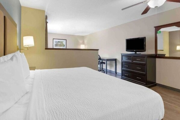A hotel room with a large bed, a television, a dresser, and a ceiling fan.