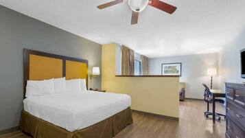 Ein Hotelzimmer mit Bett, Schreibtisch, Stuhl, Kommode, Deckenventilator und einem Fenster mit Vorhängen.