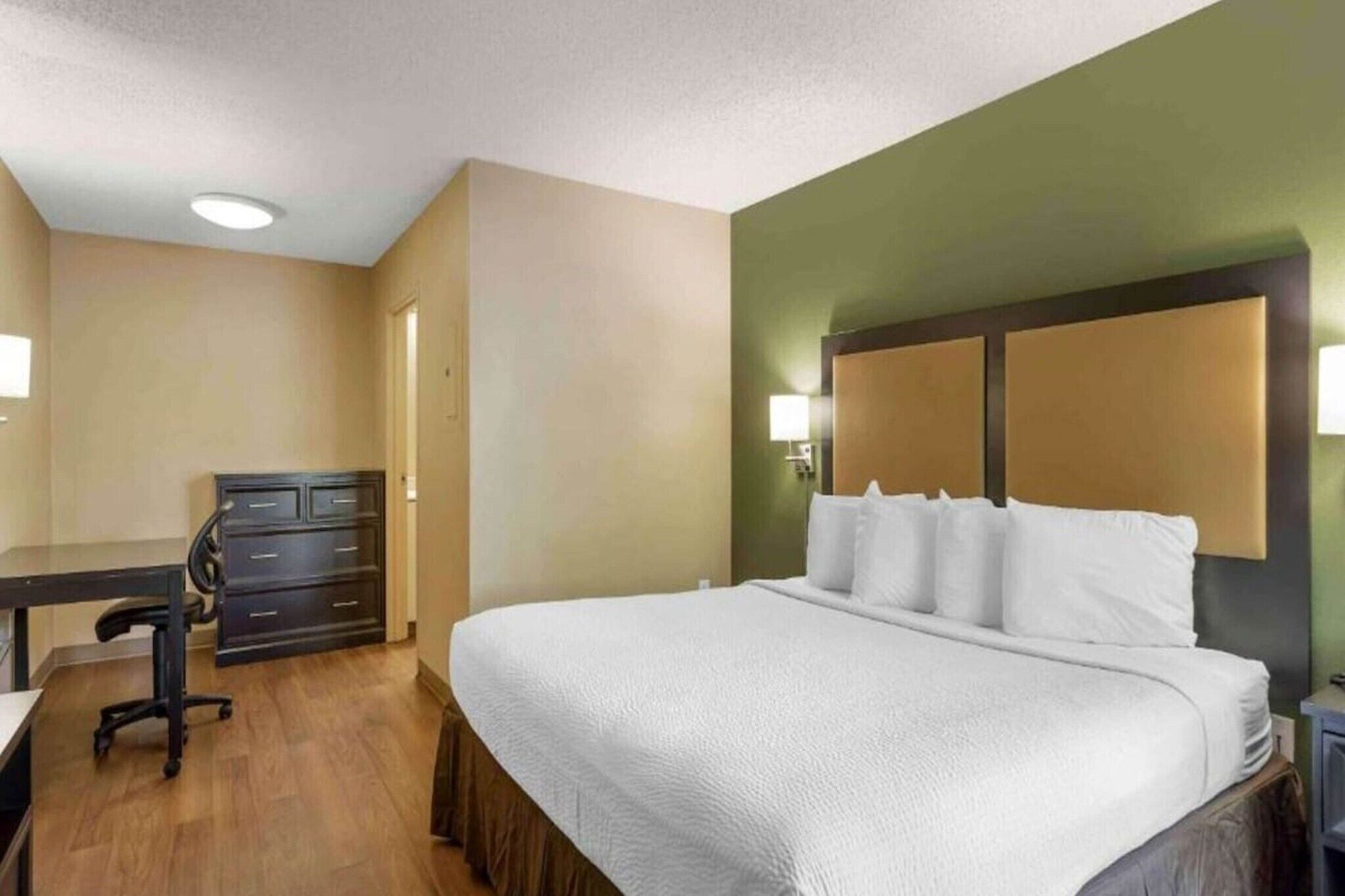 A hotel room with a bed, desk, chair, and dresser.