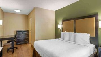A hotel room with a bed, desk, chair, and dresser.