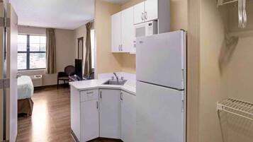 A compact hotel room with a kitchenette, a bed, a window with curtains, and a view of the outdoors.