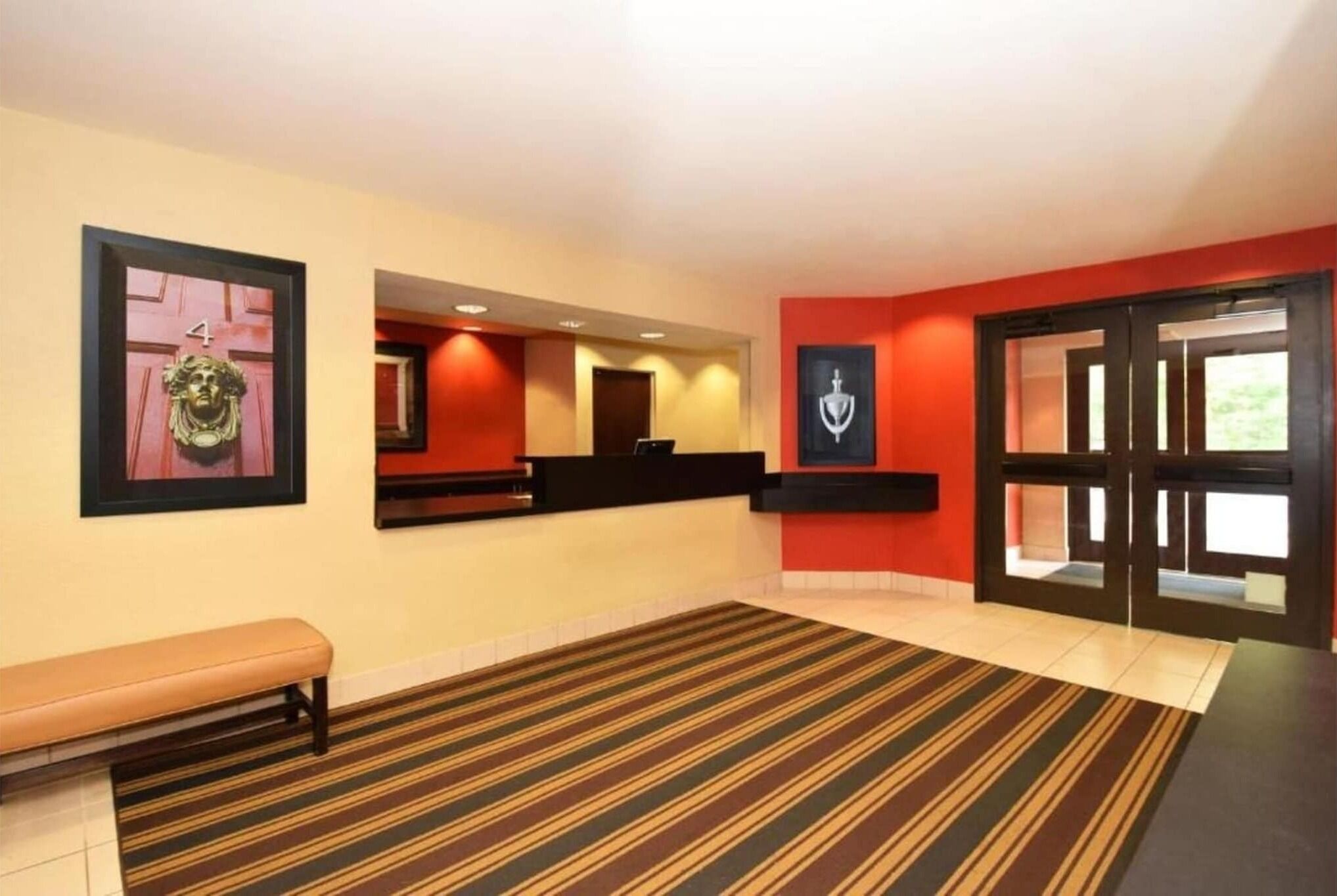 A hotel lobby with a reception desk, a bench, and a striped carpet.