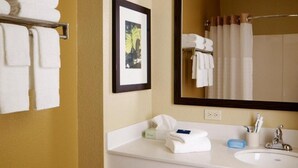 Ein Hotelbad mit einem weißen Waschbecken, einem gerahmten Bild an der Wand und Handtüchern an einem Ablagekorb.