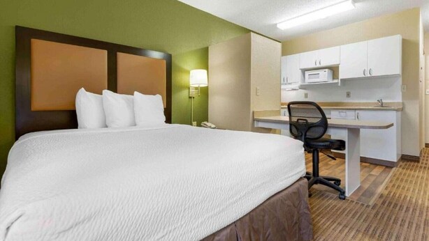 Ein Hotelzimmer mit Bett, Schreibtisch, Stuhl, Mikrowelle und Telefon.