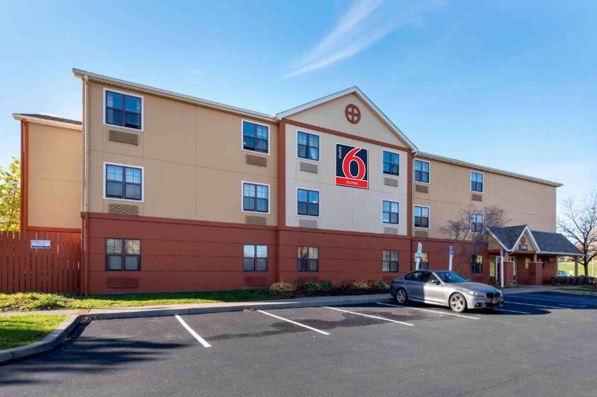 Ein mehrstöckiges Hotel mit auffälligem Logo, einem Parkplatz und einem davor stehenden Auto.