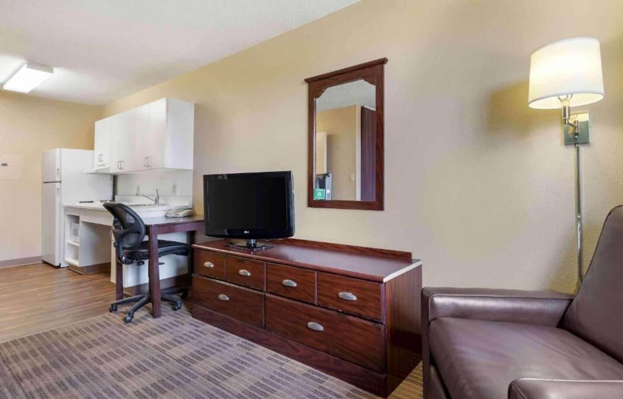 A hotel room with a desk, chair, television, dresser, and a sofa.