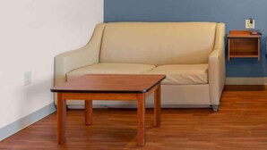 A beige sofa, a wooden coffee table, and a small wooden side table with a power outlet in a room with wooden flooring and a blue accent wall.