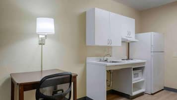 Een kitchenette met een wit aanrecht, gootsteen en een magnetron. Er is een klein tafeltje met een stoel en een wandlamp.