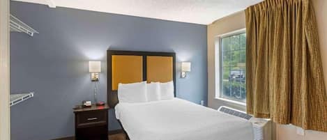 A hotel room with a bed, bedside table, lamp, and window with curtains.
