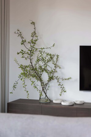 Een minimalistisch ingerichte kamer met een donkere houten console, een glazen vaas met een tak, en drie witte decoratieve objecten.