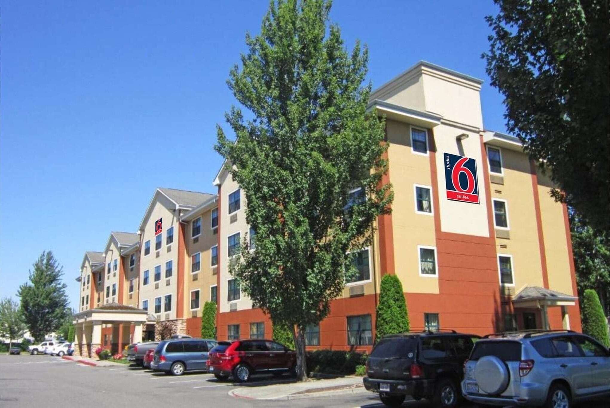 Um hotel com uma placa indicando 6 Suítes, vários andares e um estacionamento com vários carros.