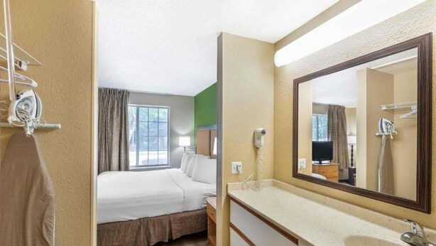 A hotel room with a bed, a bathroom with a large mirror, a sink, and a window. - 1 Queen Bed | Non-Smoking, Kitchen (Milwaukee WI)
