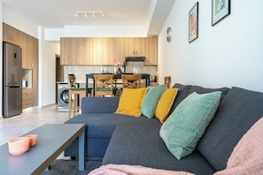 Un salon moderne avec un canapé gris, une table basse et un coin repas doté de meubles en bois, et une cuisine en arrière-plan.