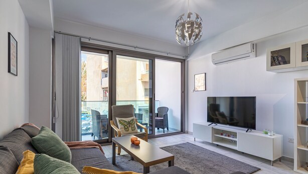 Een moderne woonkamer met een bank, salontafel, televisie en een balkon met buitenmeubilair.
