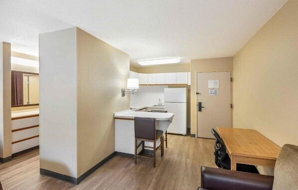 Ein kleines Hotelzimmer mit Küchenzeile, Schreibtisch, Stuhl, Tisch und einer Tür.