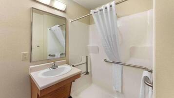 A bathroom with a sink, mirror, shower, and grab bars.
