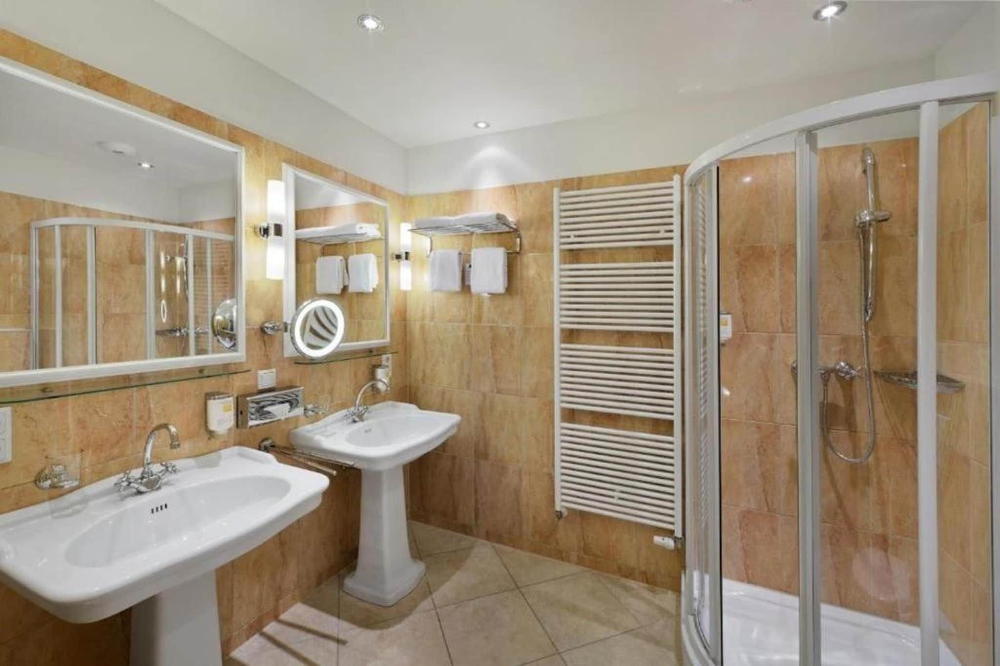 Une salle de bain moderne avec une douche à parois de verre, deux vasques, un grand miroir et un porte-serviettes.