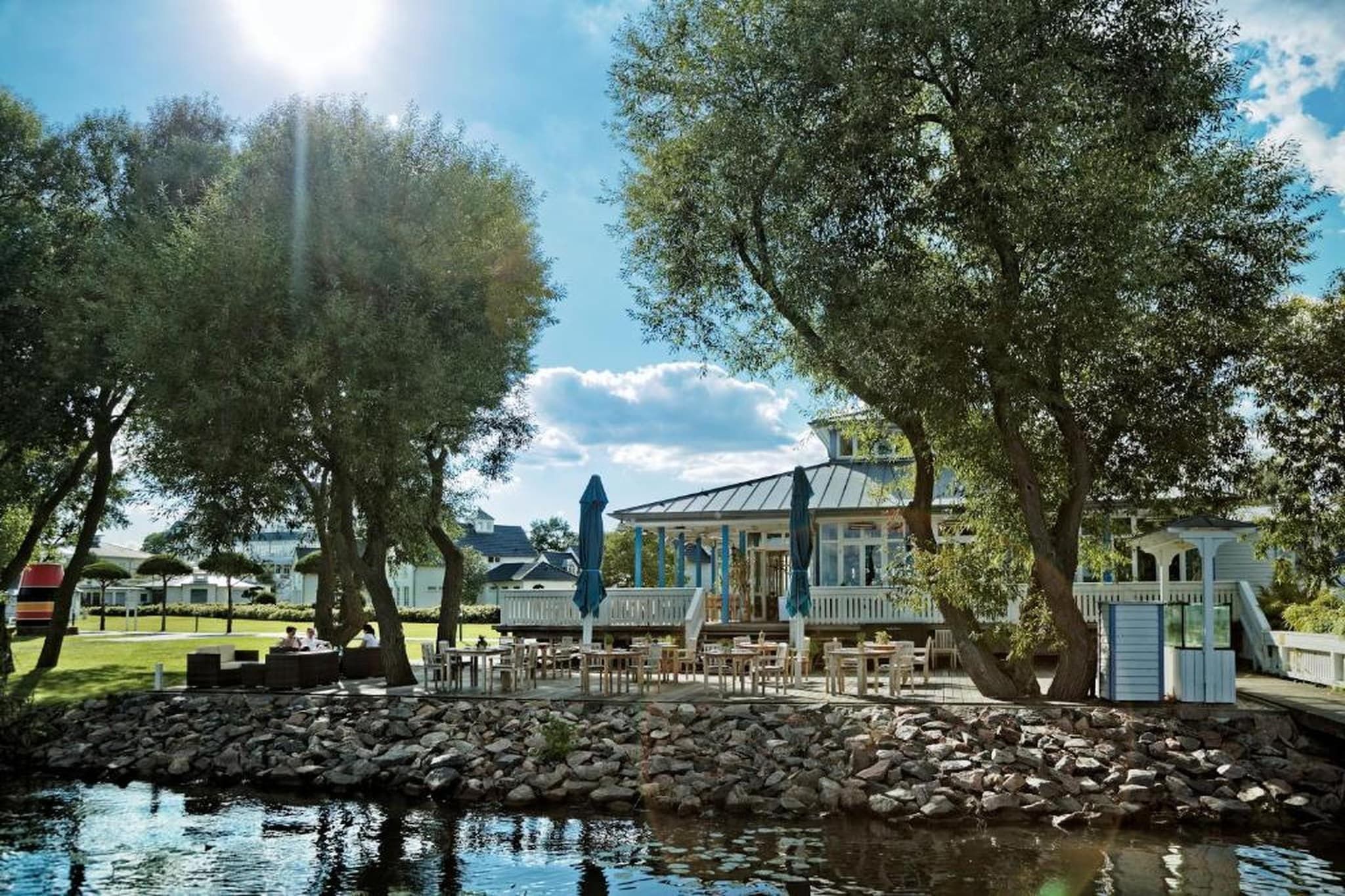 Un restaurante junto al lago con terraza al aire libre, un patio cubierto y vistas al agua.
