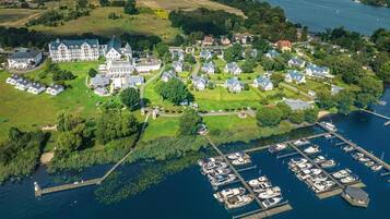 Vista aérea de una propiedad junto al lago que incluye una gran finca, casas más pequeñas y un puerto deportivo con barcos.