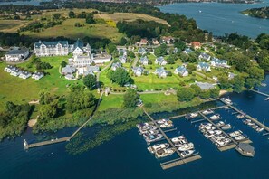 Vista aérea de una propiedad junto al lago que incluye una gran finca, casas más pequeñas y un puerto deportivo con barcos.