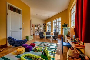 A room with a wooden floor, a white door, a bean bag chair, a small table with chairs, a bookshelf, and a window with curtains. - Schwielowsee  Hotel Superior Double Room (Werder)