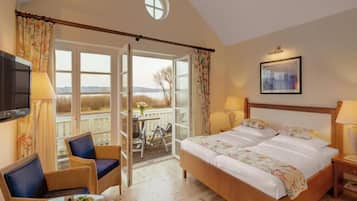 A bedroom with a large bed, two bedside lamps, a television, a chair, a table with fruit, and a balcony with a view.
