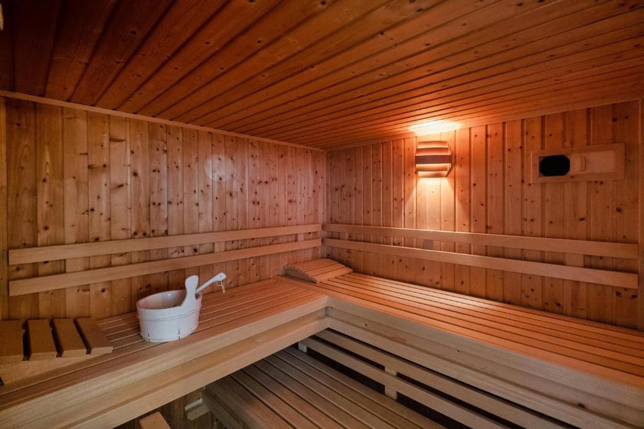 A wooden sauna with benches, a white bucket, and a wall-mounted heater.