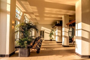 A spacious indoor corridor with a bench, potted plants, and a large circular mirror on the wall. - Schwielowsee  Hotel Superior Double Room (Werder)