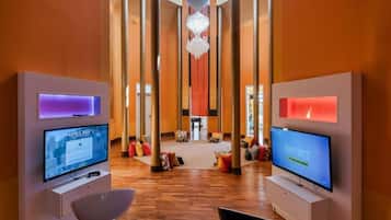 A modern lobby with two TVs displaying video games, a central chandelier, and a wooden floor.