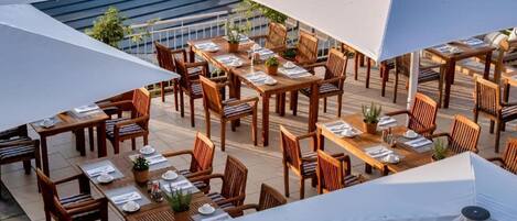 An outdoor dining area with multiple wooden tables and chairs, arranged under white canopies.