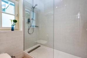 Eine Duschkabine mit weißen Fliesen, ein Fenster mit einer Pflanze und eine sichtbare Toilette.