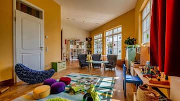 A room with a white door, a bean bag chair, a round ottoman, a puzzle on the floor, and a table with toys.